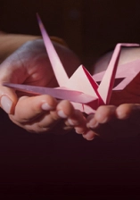 a paper crane sitting on top of open palms