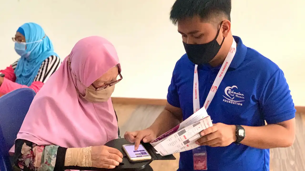 An RLAF volunteer teaching a beneficiary how to use a mobile app.